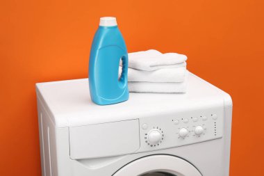 İçerideki turuncu duvarın yanındaki çamaşır makinesine bir şişe yumuşatıcı ve havlu.