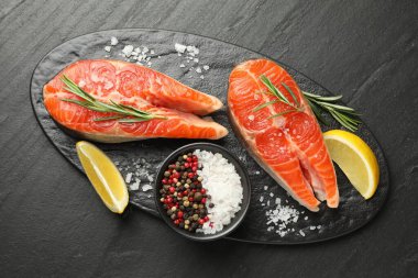 Deniz ürünleri. Siyah desenli masada somon biftekleri, baharatlar ve limon dilimleri.