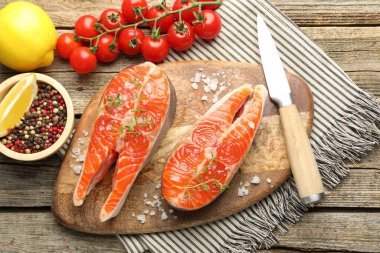 Deniz ürünleri. Somon biftekleri, baharatlar, domatesler, limonlar ve bıçaklar ahşap masada, düz yatıyordu.