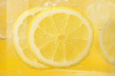 Sarı arka planda limon dilimleri ve buzla soda tazeleniyor. Yakın plan.