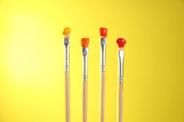 Sarı arkaplanda renk boyalı birçok fırça, yakın plan