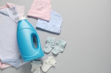 Bir şişe yumuşatıcı ve açık gri arka planda bebek kıyafetleri. Metin için boşluk