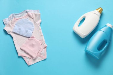 Yumuşatıcı şişeler ve açık mavi arka planda bebek kıyafetleri.