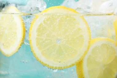 Açık mavi arka planda limon dilimleri ve buzla soda tazeleniyor. Yakın plan.