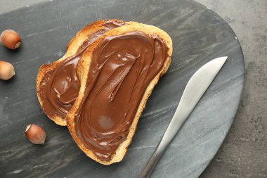 Lezzetli çikolatalı tostlar ve gri desenli masada fındıklar.