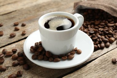 Aromatik kahve fincanda ve fasulyeler ahşap masada, yakın plan.