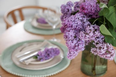Güzel leylak çiçekleri, tabaklar, çatal bıçak takımı ve cam kaplama masa, yakın plan.