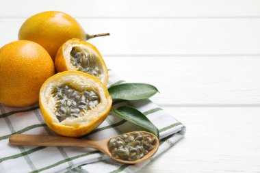 Olgun tutku meyveleri, yeşil yapraklar ve tohumlar beyaz ahşap masada, yakın plan. Metin için boşluk