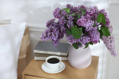Komodinin üzerinde güzel leylak çiçekleri, kahve ve kitaplar.