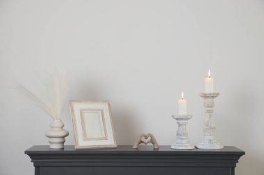 Beyaz duvarın yanındaki şöminede yanan mumlar ve diğer dekorlarla süslü şamdanlar.