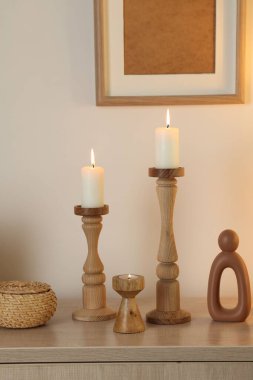 Havalı şamdanlar, yanan mumlar ve kapalı alandaki bej duvarın yanındaki dolaptaki diğer dekorlar.