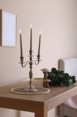 Havalı şamdanlar, yanan mumlar ve bej duvarın yanındaki ahşap masa üzerindeki diğer dekorlar.