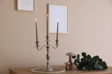 Havalı şamdanlar, yanan mumlar ve bej duvarın yanındaki ahşap masa üzerindeki diğer dekorlar.