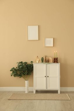 Havalı şamdanlar, yanan mumlar ve kapalı alandaki bej duvarın yanındaki dolaptaki diğer dekorlar.