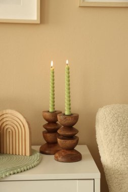 Havalı şamdanlar, yanan mumlar ve kapalı alandaki bej duvarın yanındaki dolaptaki diğer dekorlar.