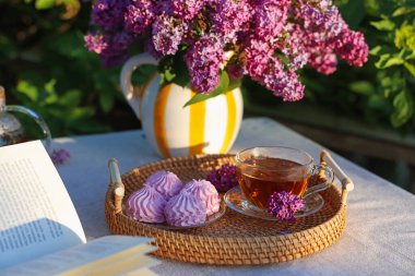 Bahçedeki masada güzel leylak çiçekleri, çay, zephyrler ve kitap.