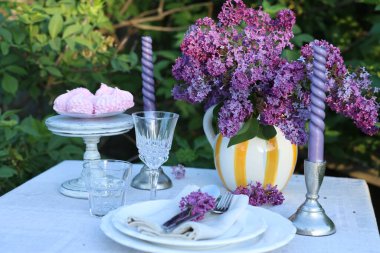 Güzel leylak çiçekleri, zephyrler, tabaklar, çatal bıçaklar, bardaklar ve mumlar bahçede.