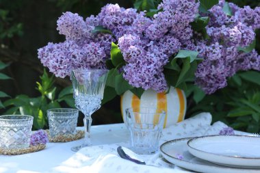 Güzel leylak çiçekleri, tabaklar, bardaklar, kaşıklar ve mumlar bahçede.