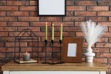 Mum ve tuğla duvarın yanındaki masada yanan mumlar.