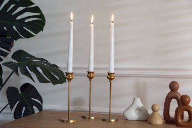 Beyaz duvarın yanındaki masada yanan mumlarla şamdanlar.