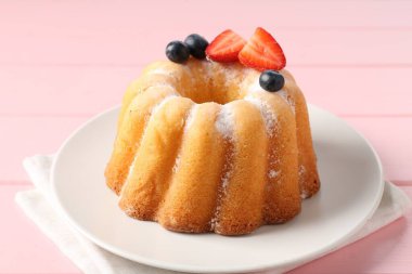 Pembe ahşap masada pudra şekeri ve böğürtlenli Lezzetli kek, yakın plan.