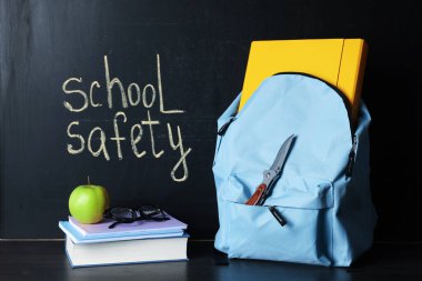 Sırt çantasında bıçak, kitap, defterler, bardaklar ve elma tahtaya yakın siyah tahta masada. Okul güvenliği