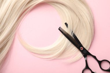 Açık pembe zemin üzerinde saç teli ve makas, üst görünüm