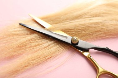 Açık pembe arka planda saç teli ve makas, yakın plan.