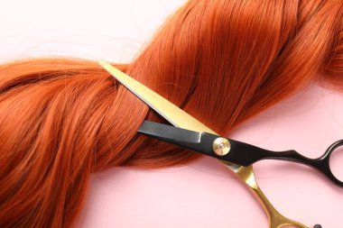 Açık pembe arka planda saç teli ve makas, yakın plan.