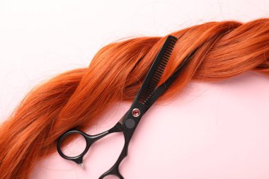 Açık pembe zemin üzerinde saç teli ve makas, üst görünüm