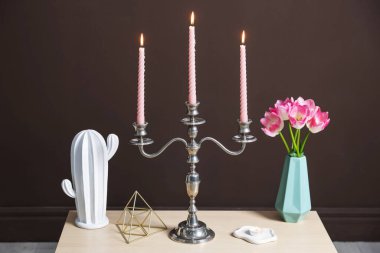 Kahverengi duvarın yanında yanan mumlar ve dekorlarla süslü zarif bir şamdan.