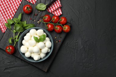 Lezzetli mozzarella peyniri topları kasede, fesleğende, biberlikte ve domateslerde siyah masada, üst tarafta. Metin için boşluk