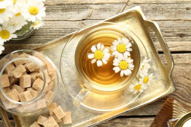 Cam fincanda nefis papatya çayı, taze çiçekler ve ahşap masada kahverengi şeker, düz uzanmış.