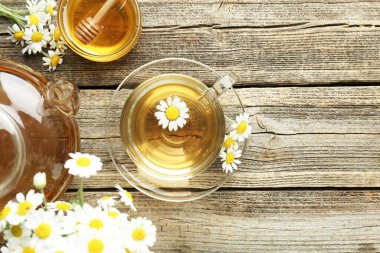 Cam bardakta nefis papatya çayı, taze çiçekler, ahşap masada bal ve çaydanlık, düz yatak. Metin için boşluk