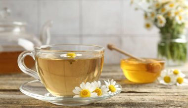 Cam bardakta nefis papatya çayı, taze çiçekler, ahşap masada bal ve çaydanlık, yakın plan.