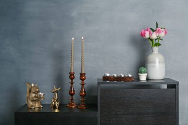Zarif şamdanlar yanan mumlar vazoda laleler ve gri duvarın yanındaki dolapta diğer dekorlar.