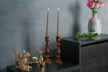 Zarif şamdanlar yanan mumlar vazoda laleler ve gri duvarın yanındaki dolapta diğer dekorlar.