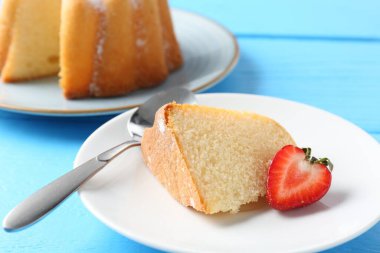 Açık mavi ahşap masada çilekli bir dilim lezzetli kek, yakın plan.