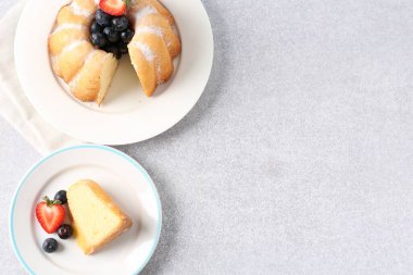 Açık gri masada pudra şekeri ve böğürtlenli leziz bir kek. Metin için boşluk