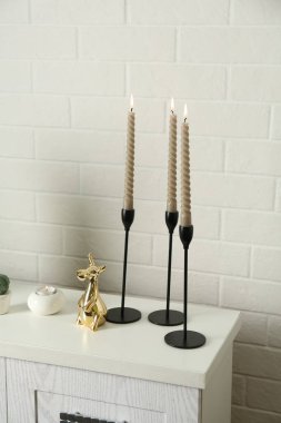 Beyaz tuğla duvarın yanındaki şifoniyerde yanan mumlar ve diğer dekorlar olan zarif şamdanlar.