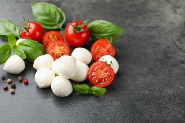 Mozzarella peyniri, domates, fesleğen ve biberler gri masada, yakın plan.