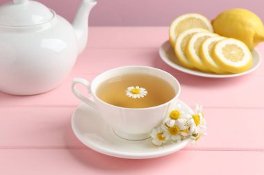 Fincanda nefis papatya çayı, taze çiçekler ve pembe ahşap masada limon, yakın plan.