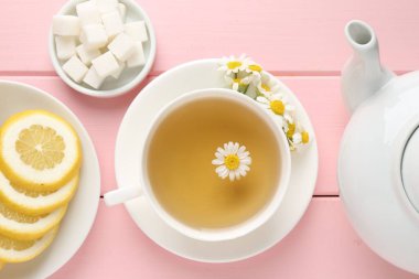 Fincanda nefis papatya çayı, taze çiçekler, şeker küpleri ve pembe ahşap masada limon.