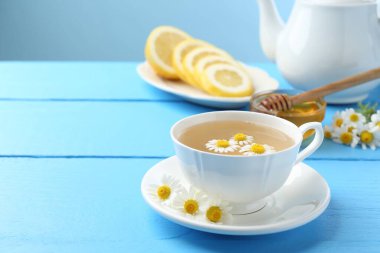 Fincanda nefis papatya çayı, taze çiçekler, açık mavi ahşap masada limon ve bal, yakın plan. Metin için boşluk