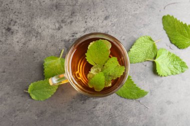 Cam bardakta Aromatik limon merhemi çayı ve gri desenli masada taze yapraklar.