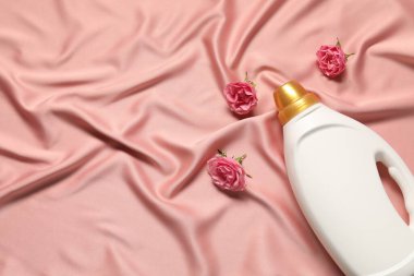 Bir şişe yumuşatıcı ve pembe kumaş üzerinde çiçekler, düz yatak. Metin için boşluk