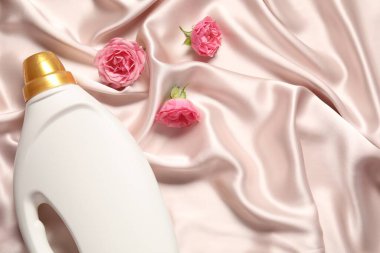 Bir şişe yumuşatıcı ve bej kumaşlı çiçekler, düz yatak. Metin için boşluk