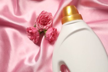 Bir şişe yumuşatıcı ve pembe kumaş üzerinde çiçekler.