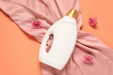 Bir şişe yumuşatıcı, çiçekler ve mercan zemin üzerinde pembe kumaş, düz uzanmış.