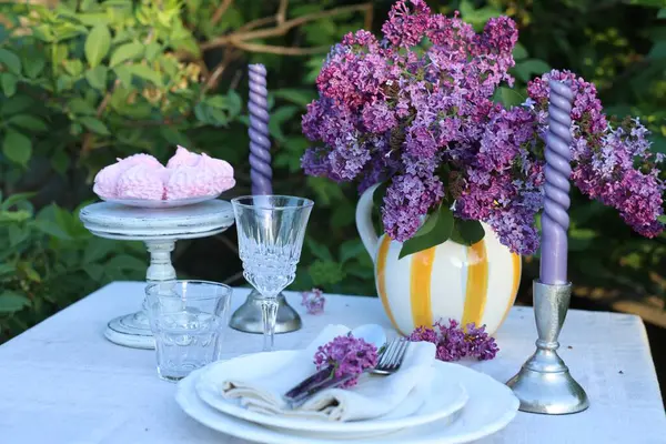 Güzel leylak çiçekleri, zephyrler, tabaklar, çatal bıçaklar, bardaklar ve mumlar bahçede.